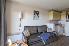 Ein Wohnzimmer mit Sofa, Lampe, Küchenzeile und einer Wand mit einem Poster.