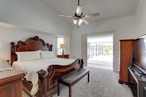 A bedroom with a wooden bed, a bench, a ceiling fan, a TV, and a large window. - Patio & Grill! Canalfront Rotonda West Golf Escape (Rotonda West)