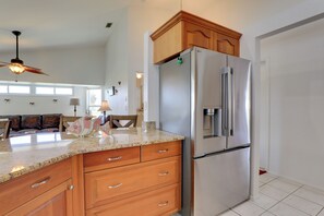 A kitchen with a stainless steel refrigerator, wooden cabinets, a granite countertop, and a ceiling fan. - Patio & Grill! Canalfront Rotonda West Golf Escape (Rotonda West)