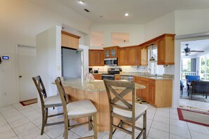 A kitchen with wooden cabinets, a central island, and a dining area with chairs. - Patio & Grill! Canalfront Rotonda West Golf Escape (Rotonda West)