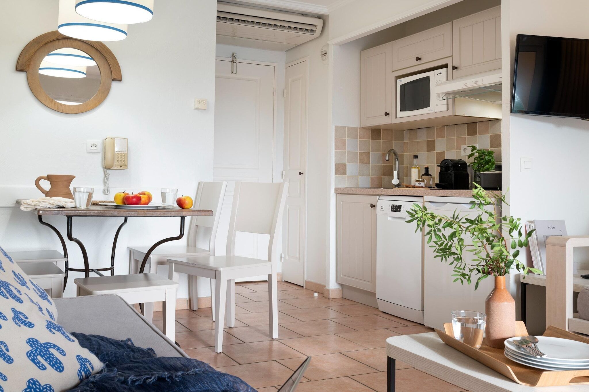 Une cuisine moderne avec des meubles blancs, un four à micro-ondes et une machine à café. On y trouve une table à manger avec des chaises et un vase avec une plante.