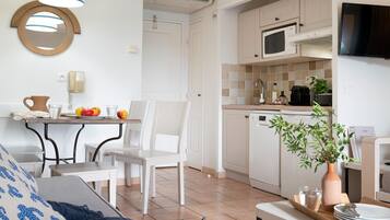 Une cuisine moderne avec des meubles blancs, un four à micro-ondes et une machine à café. On y trouve une table à manger avec des chaises et un vase avec une plante.