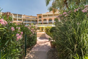 A courtyard with a pathway leading to a building with multiple balconies and a covered seating area. - Luxury 4-Person Riviera Sanctuary (Les Issambres)