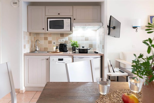 A compact kitchen with white cabinetry, a microwave, a coffee maker, and a small dining area with a table and chairs.