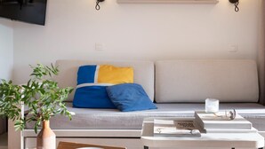 Ein modernes Wohnzimmer mit einer Couch, einem Couchtisch, einer Pflanze und einem Flachbildfernseher.