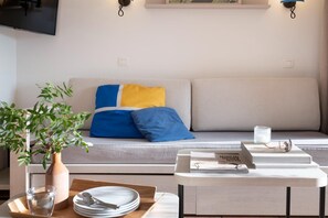 A modern living room with a sofa, a coffee table, a plant, and a flat-screen TV.