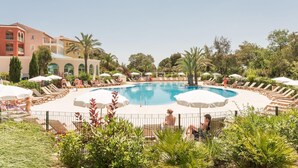 Ein Poolbereich mit Liegestühlen und Sonnenschirmen, umgeben von Pflanzen und Gebäuden.