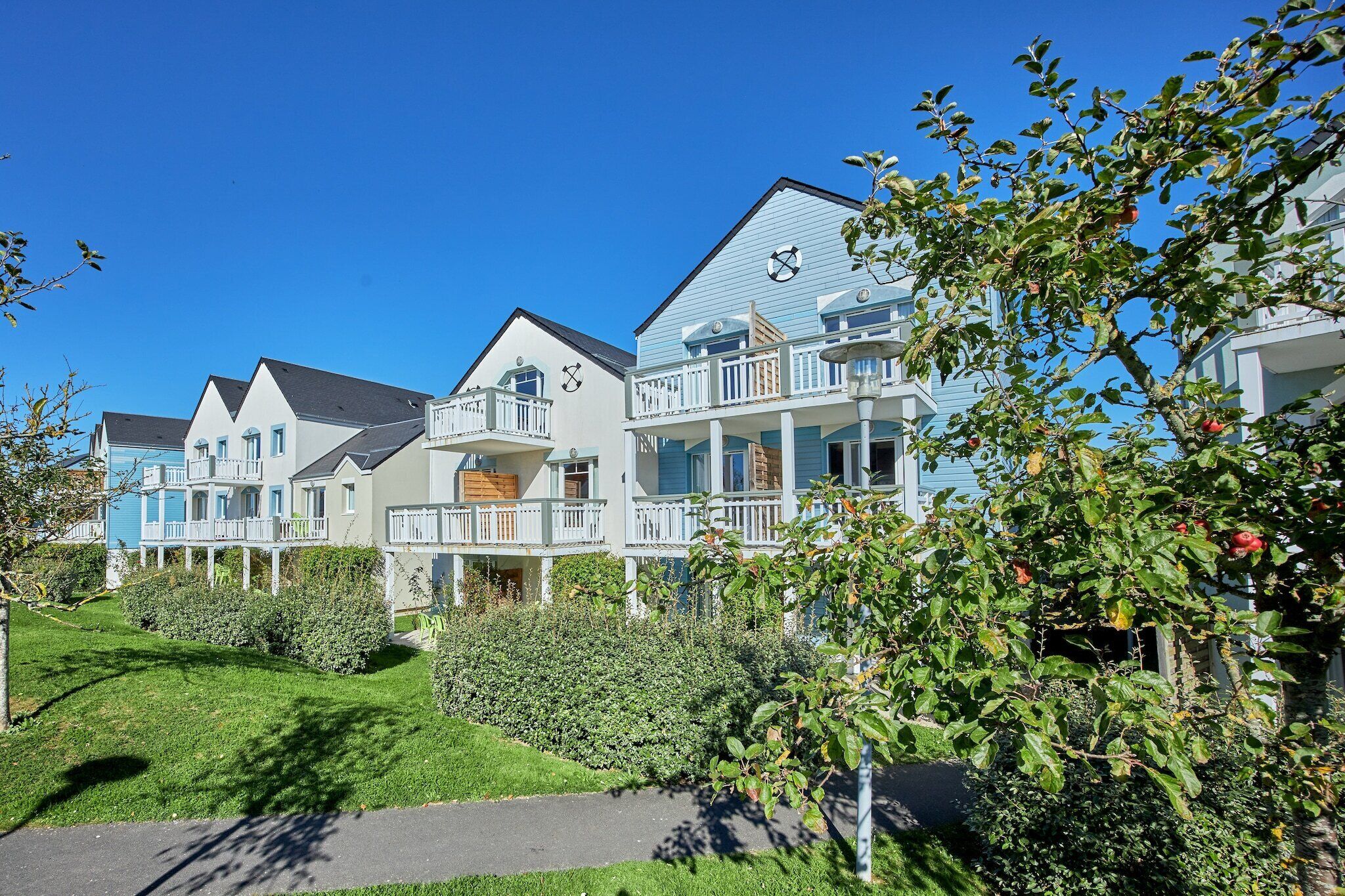 Een rij moderne, twee verdiepingen tellende huizen met balkons, een verzorgd gazon en een heldere blauwe lucht.