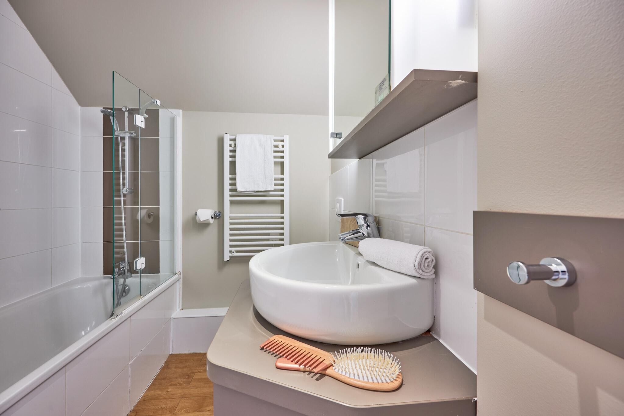 A bathroom with a glass shower enclosure, a white sink, and a towel rack.