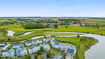 Een woonwijk met huizen aan een rivier, een parkeerplaats en groene velden.