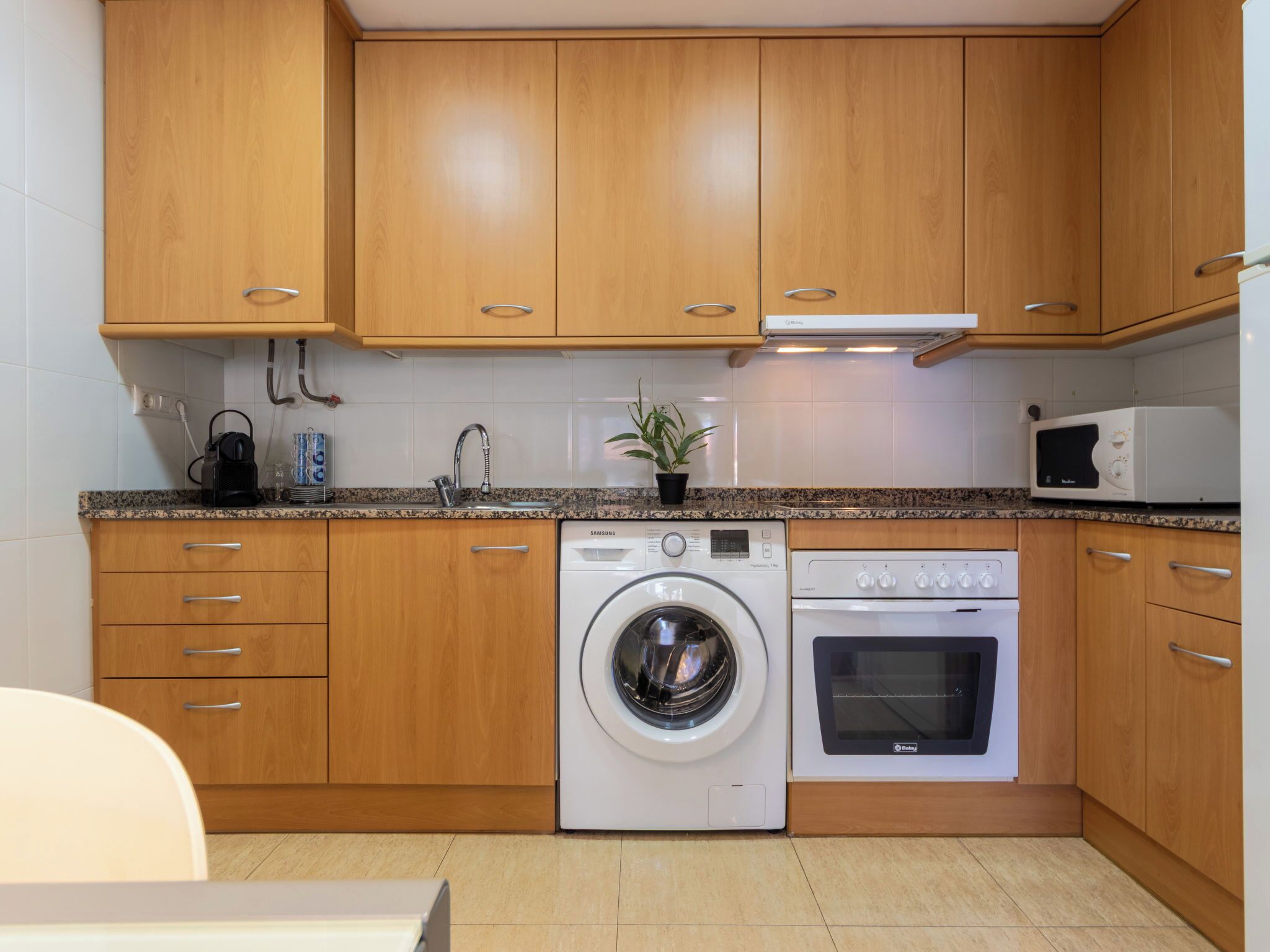 Une cuisine compacte avec des meubles en bois, un lave-linge, un four et un four à micro-ondes.