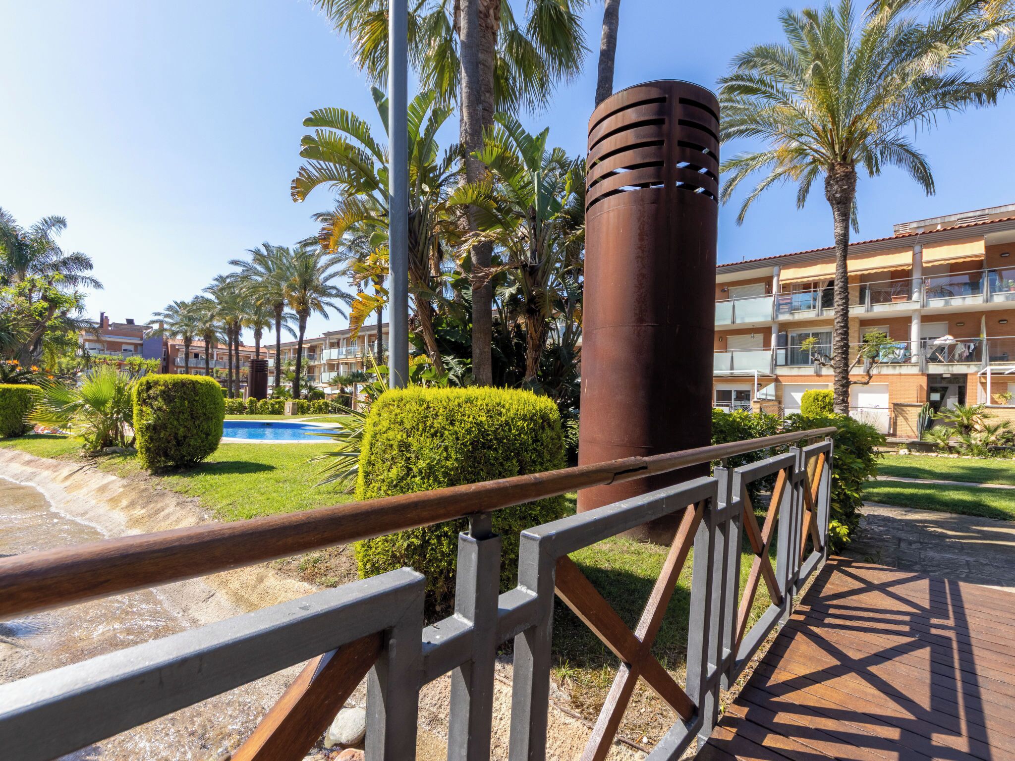 A hotel with a pool, palm trees, and a metal fence.