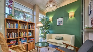 Ein gemütliches Wohnzimmer mit grüner Wand, einer Bücherwand, einem Sofa und einem Korbstuhl.