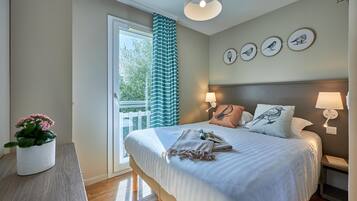 Une chambre à coucher avec un lit, des lampes de chevet, une table de chevet, une fenêtre avec des rideaux, une plante en pot et des œuvres d’art mural.