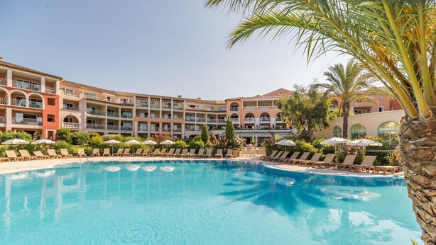 Et hotel med en stor swimmingpool, liggestole og en palme.