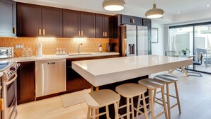 Uma cozinha moderna com armários escuros, eletrodomésticos de aço inoxidável, uma ilha grande com banquetas e iluminação pendente.