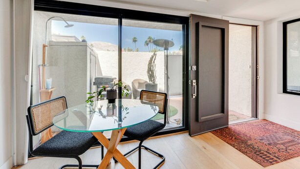 Quarto moderno com mesa de vidro, duas cadeiras, uma porta e vista para paisagem desértica.