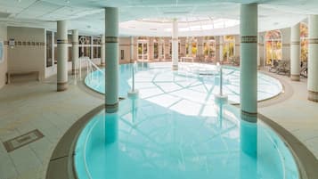 Una amplia piscina interior con una fuente central, rodeada de columnas e iluminada por luz natural.