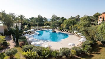 Ein kreisförmiger Pool mit Liegestühlen und Sonnenschirmen, umgeben von Grünflächen und einem Gebäude.