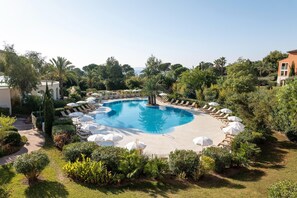 Une piscine circulaire entourée de verdure et d’un bâtiment, avec des chaises longues et des parasols.