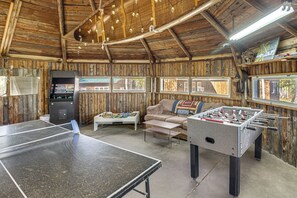 A room with a ping pong table, foosball table, and a foosball table with a view of the outdoors.