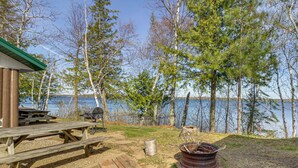 Un camping junto al lago con mesas de picnic, un pozo para fogatas y una cabaña.
