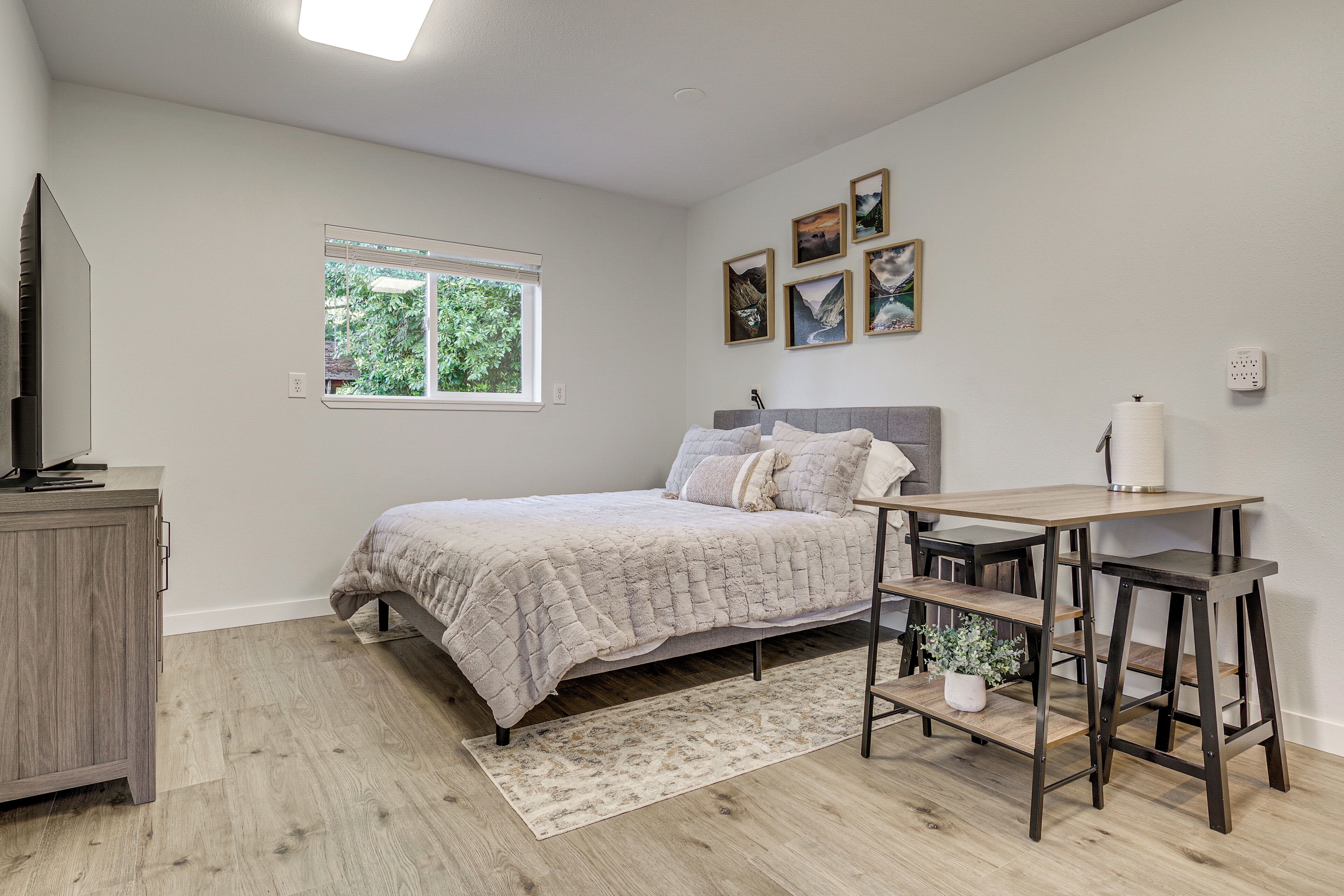 Ein Schlafzimmer mit Bett, Schreibtisch, Stuhl, Fernseher und Fenster.