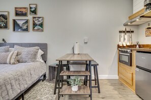 A bedroom with a bed, a small table with a plant, and a kitchen with a stove and refrigerator.