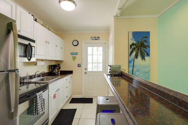 A compact kitchen with white cabinets, a stainless steel refrigerator, a microwave, and a coffee maker. - Bikes Provided! Central Condo w/ Pool in Key West (Key West)