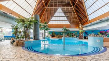 Une piscine intérieure dotée d’un sol en pierre, de poutres en bois et de plantes tropicales.