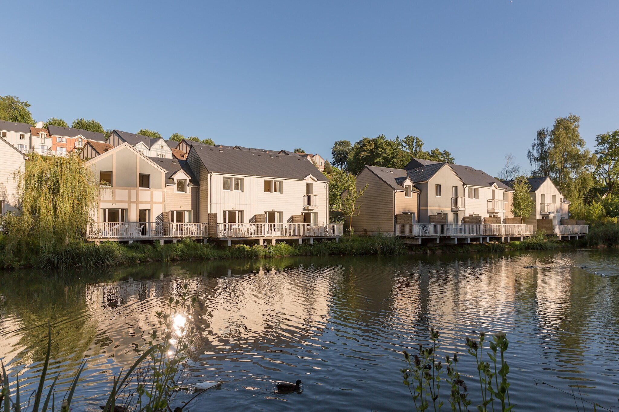 Une rangée de maisons modernes dotées de balcons, un lac paisible et un ciel dégagé.
