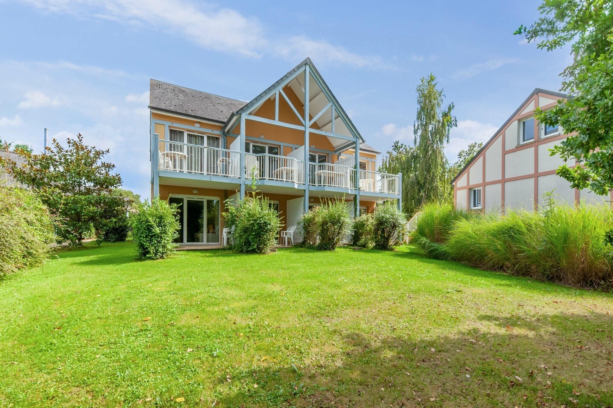 Une maison à deux étages dotée d’un balcon, entourée d’une pelouse bien entretenue et d’arbres.