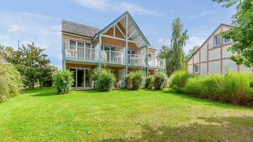 Une maison à deux étages dotée d’un balcon, entourée d’une pelouse bien entretenue et d’arbres.