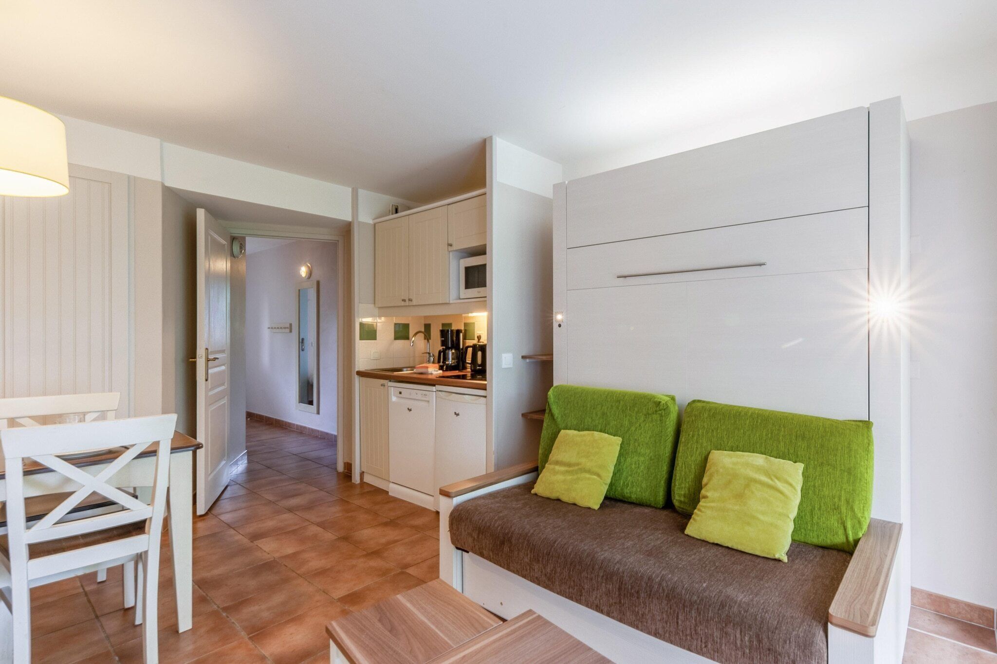 Een ruimtelijk ingerichte leefruimte met een kitchenette, een eethoek en een bank met groene kussens.