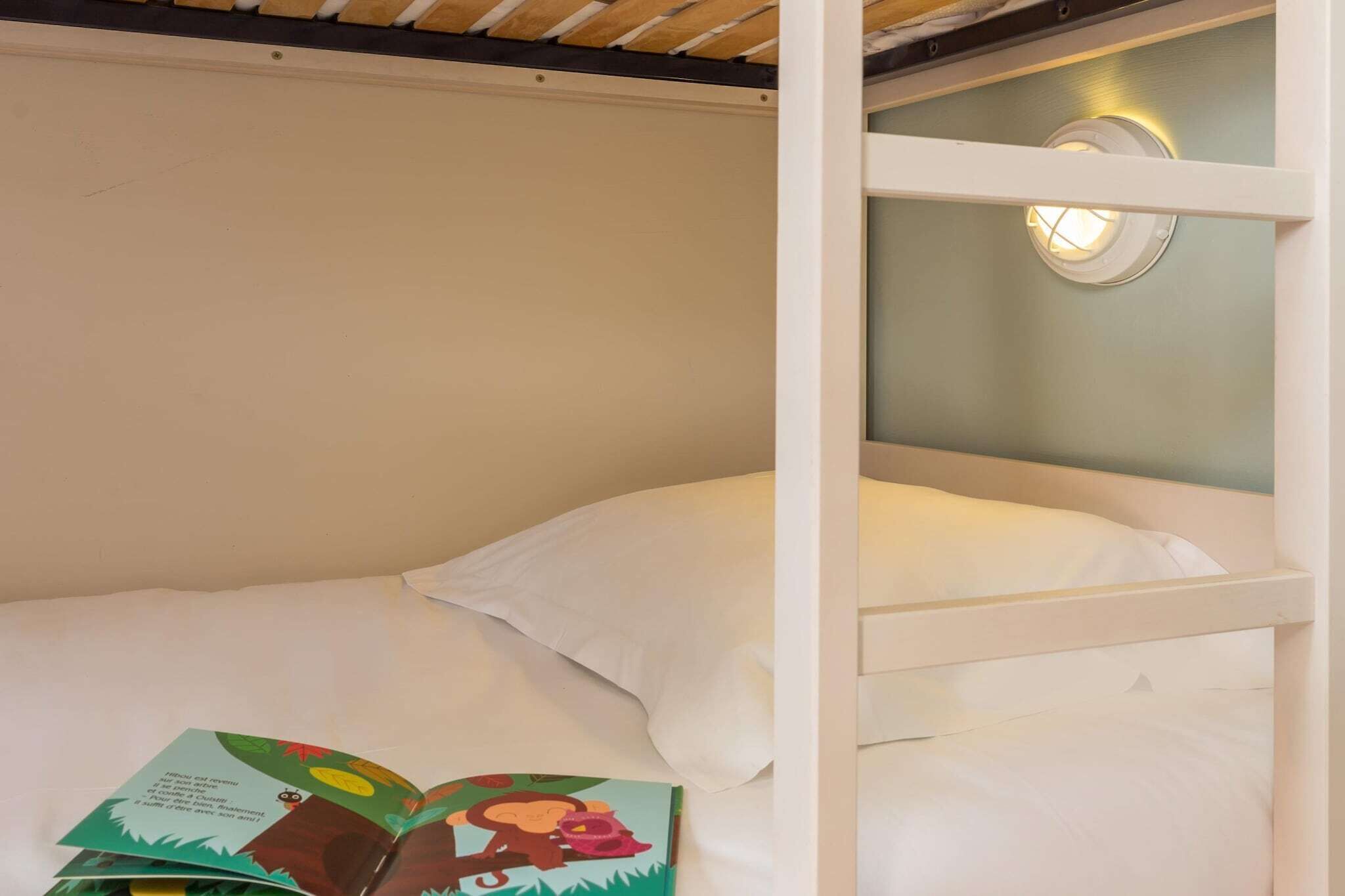 A bunk bed with a ceiling light fixture, a white pillow, and a book on the lower bunk.