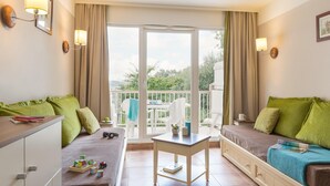 A room with a bed, a desk, a table, and a balcony with a view.