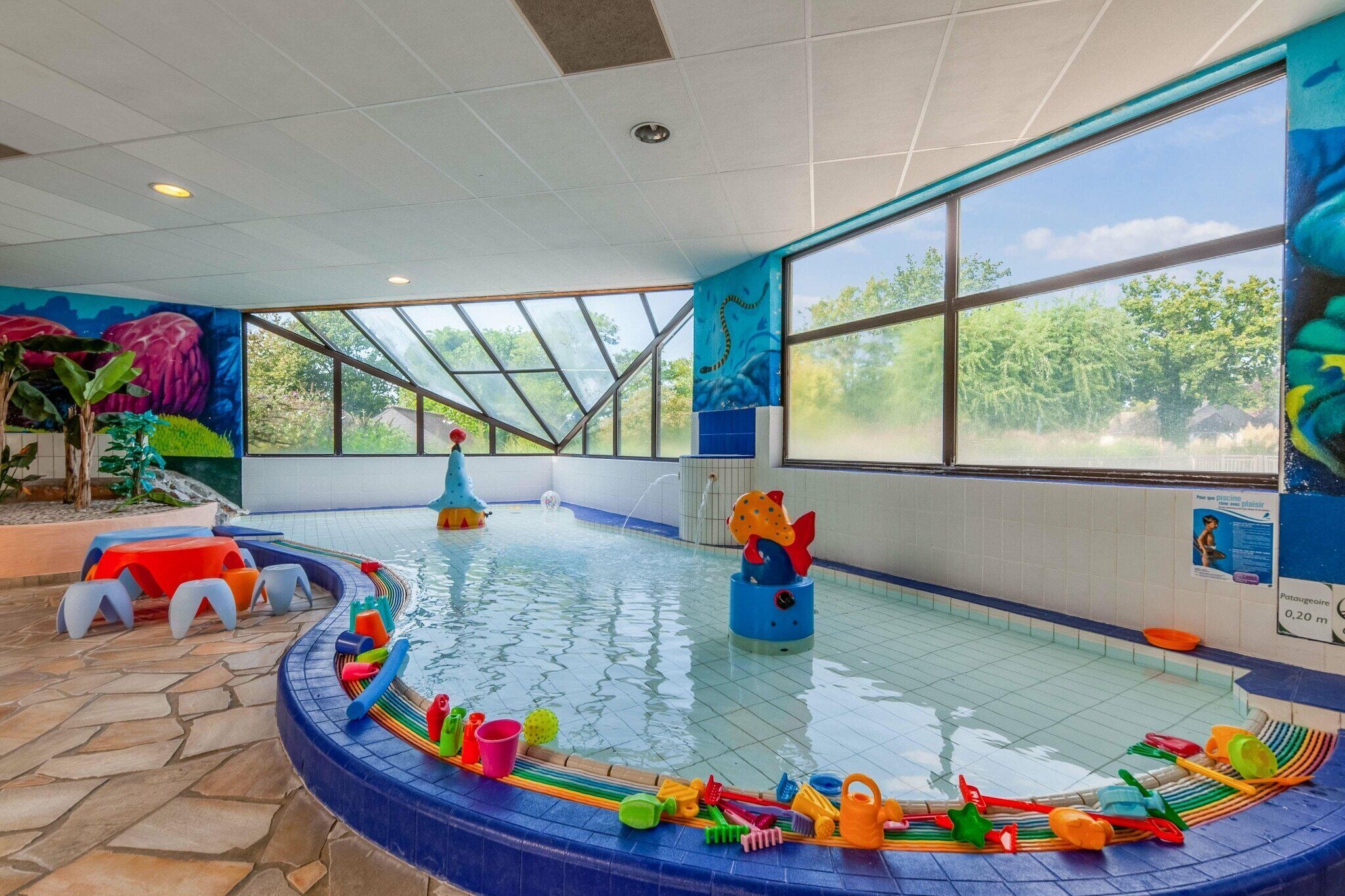 Ein Hallenbad mit klaren Glaswänden, einer blauen Poolkante und bunten Spielzeugen.