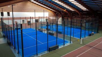 Un court de tennis intérieur, doté d’un filet, entouré d’une clôture et surmonté d’une structure de toit.