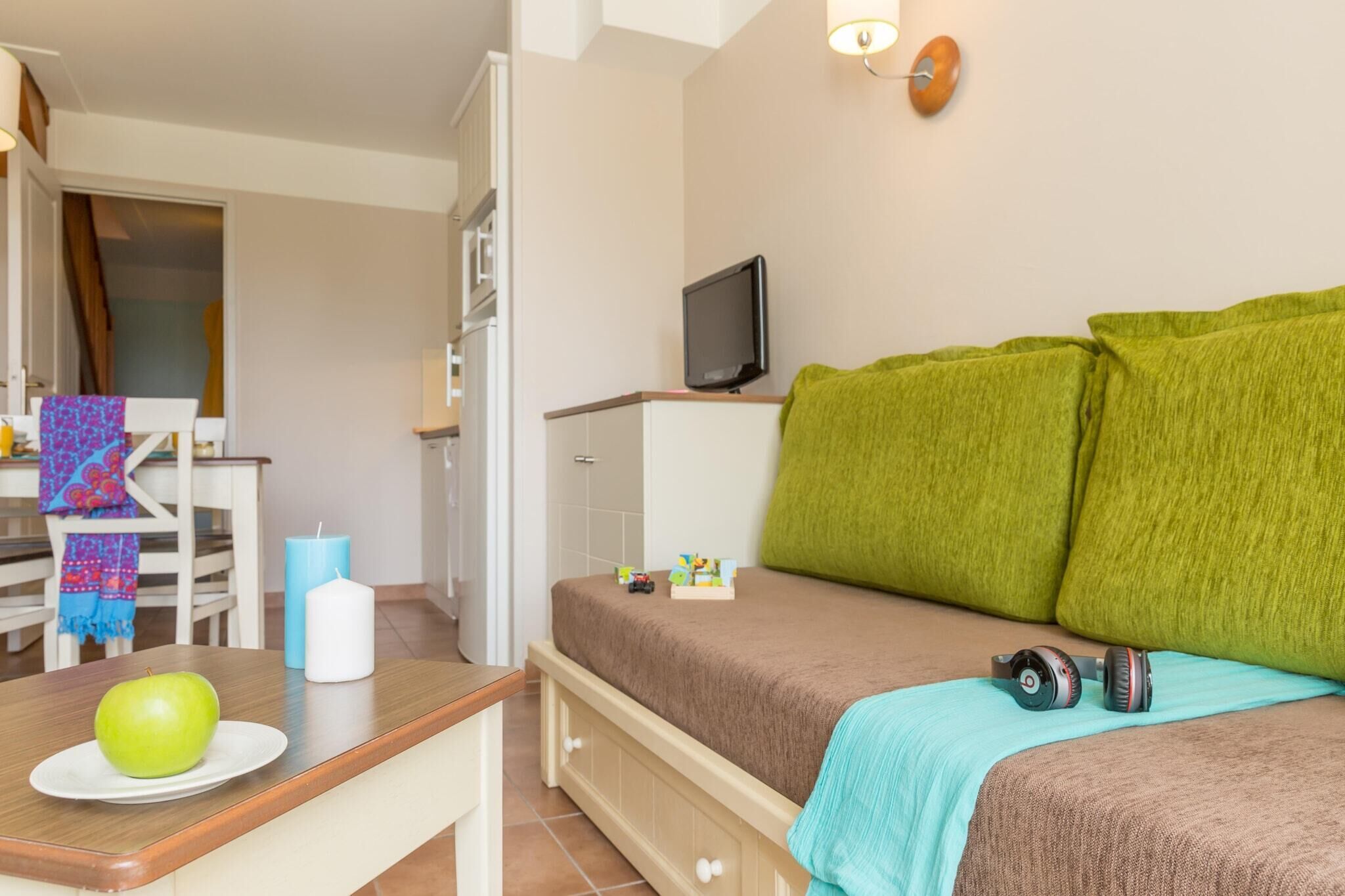 A bedroom with a bed, a TV, a table with an apple, and a chair with a towel.