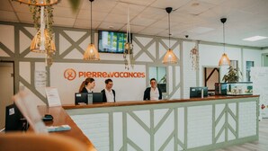A reception desk with a sign reading 'Pierre & Vacances,' two staff members behind it, and a television mounted on the wall.