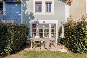 A patio with a table and chairs, a small umbrella, and a window with curtains. - Bourgenay Flat near Coastal Slopes (Talmont Saint Hilaire)