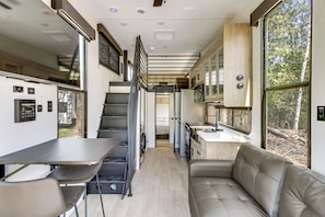 Cocina compacta con estufa, lavaplatos y armarios, un comedor con mesa y sillas, y una sala de estar con sofá.