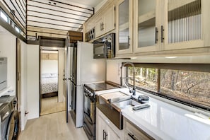 Cocina compacta con refrigerador, horno, microondas y ventana con vista a árboles.