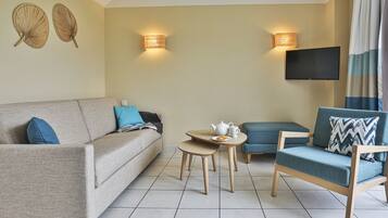 A living room with a sofa, a small table with a teapot, a blue armchair, and two wall-mounted lamps.