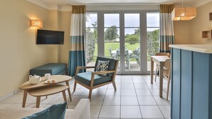 A room with a television, a table with a teapot and cups, a sofa, a chair, and a view through a glass door to an outdoor area with a table and chairs. - Holiday House near Lake & Sea (Talmont Saint Hilaire)