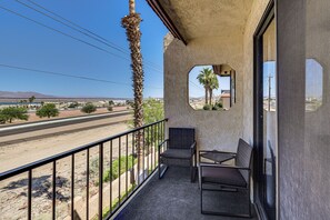 Ein Balkon mit Blick auf eine Straße und Berge, eine Palme sowie Gartenmöbel.