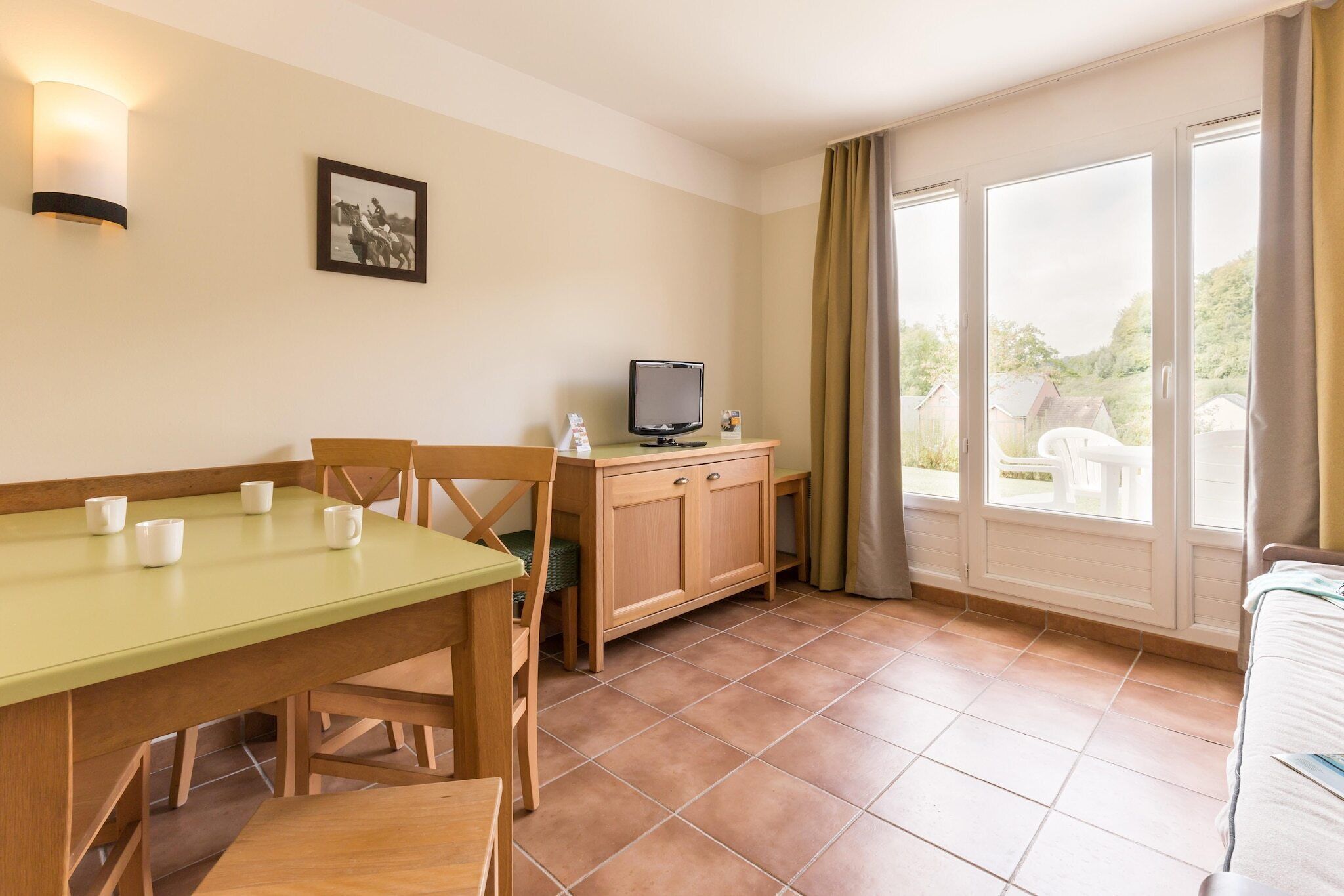 A room with a dining table, chairs, a television, and a window with curtains.