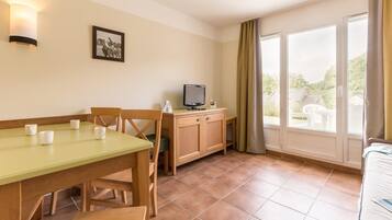 A room with a dining table, chairs, a television, and a window with curtains.