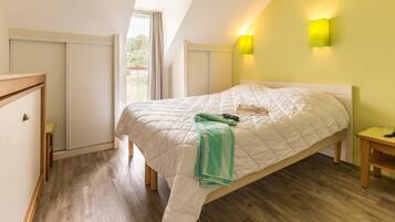 Un dormitorio con cama, mesita de noche, ventana con cortinas y lámpara de pared.