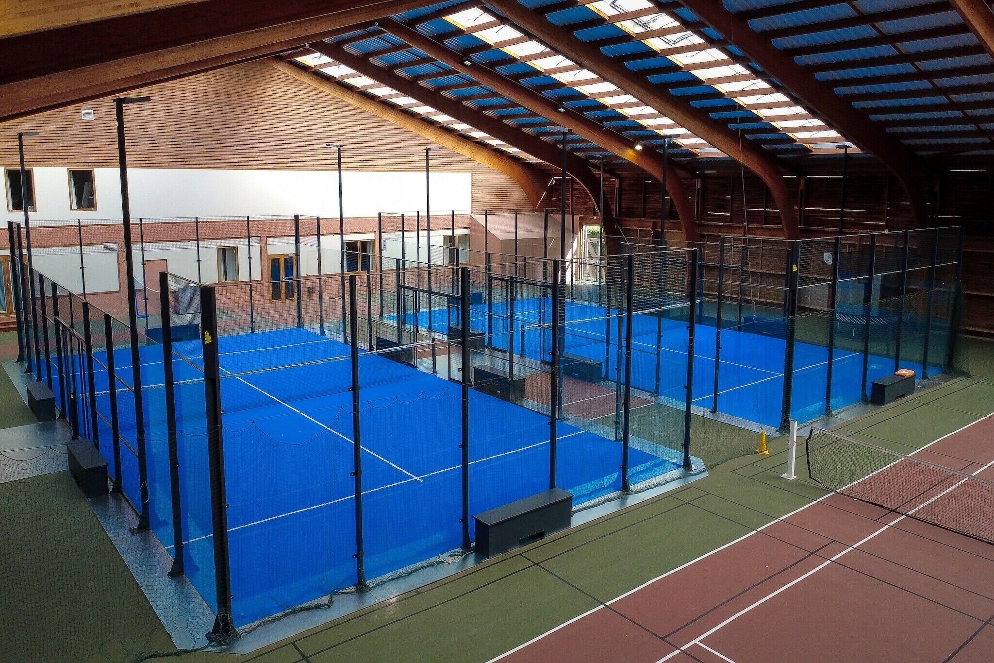 En indendørs tennisbane med net, omkranset af et hegn og en tagkonstruktion.